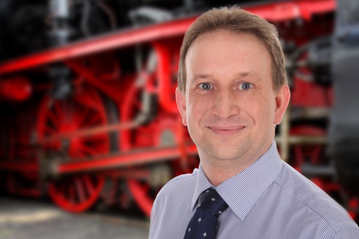 Porträtfoto von Lars Naumann vor dem Triebwerk einer Dampflokomotive
